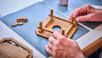 Hände montieren Holzpuzzle auf Tisch.