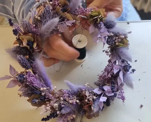 Hände fertigen einen Blumenkranz drinnen.