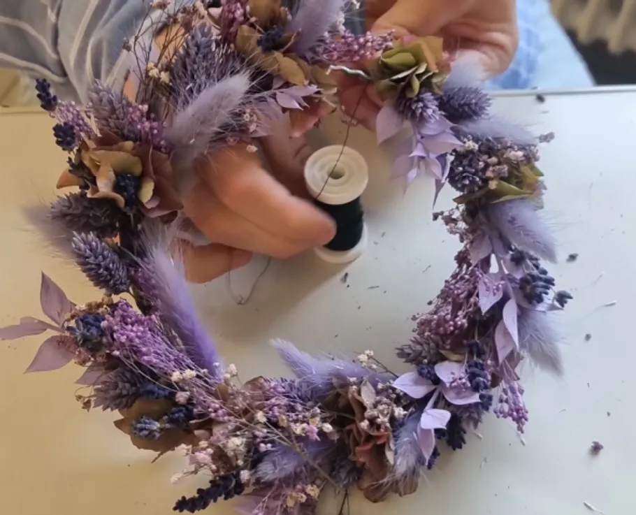 Hände fertigen einen Blumenkranz drinnen.