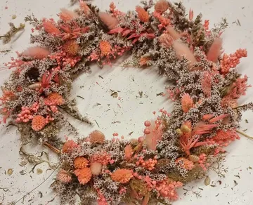 Blumenkranz auf weißer Fläche, mit verstreuten Blütenblättern.