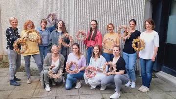 Frauen mit Kränzen draußen an der Wand.