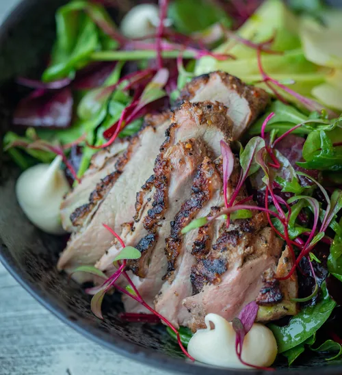 Sliced grilled meat on fresh green salad.