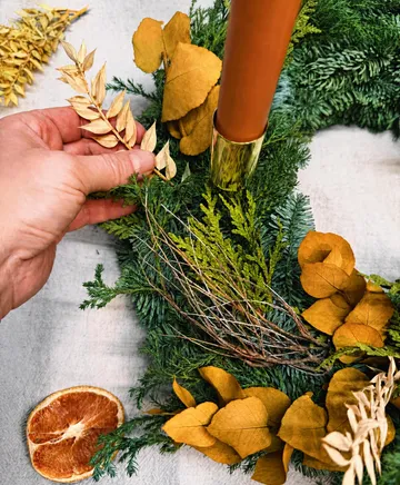 Hand arranging leaves on a decorative wreath.