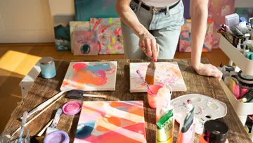 Artist painting colorful canvases on wooden table.