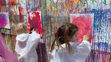 Kinder malen an bunter Spritzwand.