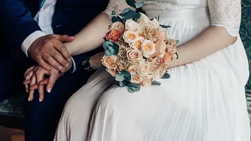 Braut hält Blumenstrauß, Bräutigam hält ihren Arm.