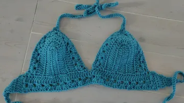 Blue crocheted bikini top on wooden floor.