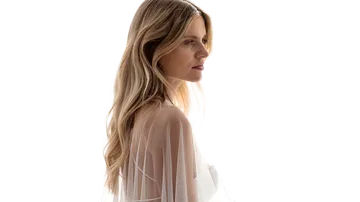 Woman in sheer blouse, side view, white background.
