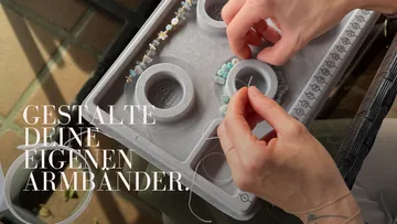 Hände fädeln Perlen auf grauem Perlenbrett.