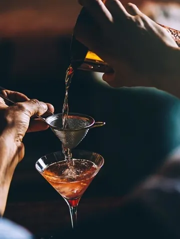 Person pouring cocktail into martini glass.