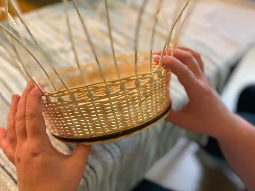 Hands weaving a basket in room.
