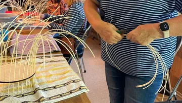 Person weaving basket in classroom setting.
