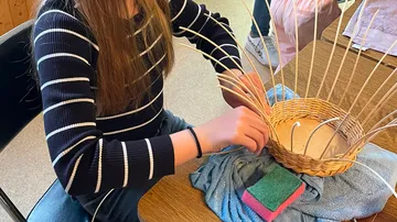Person weaving basket at a table.