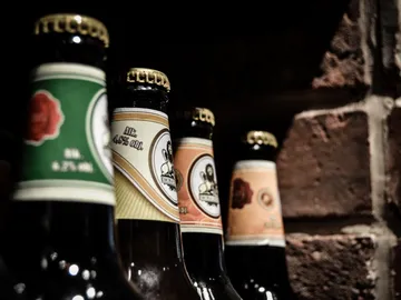 Bottles stand on a shelf in front of a brick wall.
