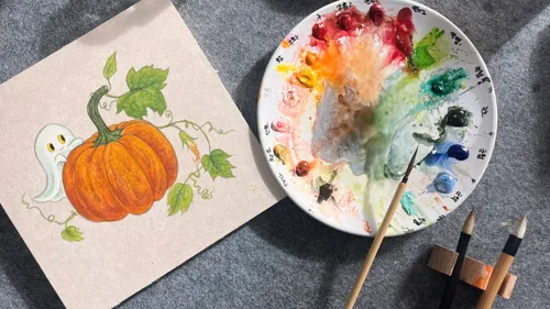 Watercolor palette and pumpkin drawing on table.