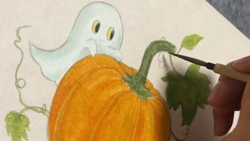 Hand paints ghost on pumpkin drawing.