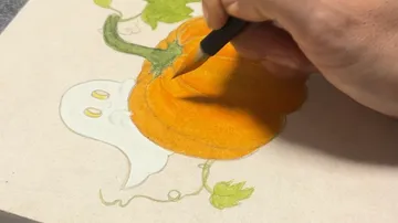 Hand draws pumpkin and ghost on paper.