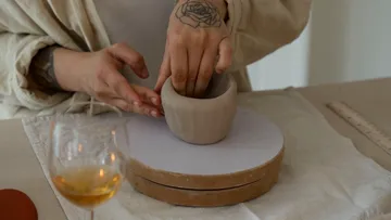 Hands shaping clay pot on table.
