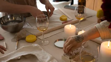 Hands crafting with candles and wine nearby.