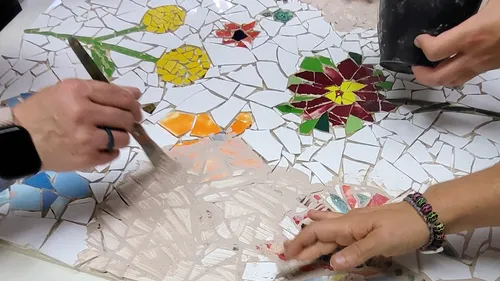 Hands working on colorful tile mosaic.