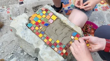 Hands placing colorful tiles on stone.
