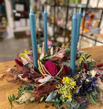 Four blue candles in floral wreath on table.