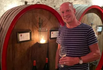Man holding wine glass by barrels.