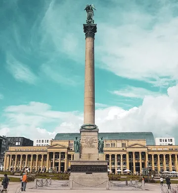 Column with angel stands in front of a historic building.