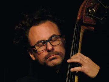 A musician passionately plays a double bass in the dark.