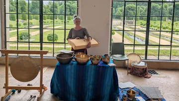 Frau spielt Instrument drinnen, Garten draußen.
