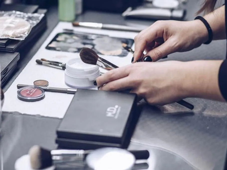 Hände arbeiten mit Make-up-Pinseln auf einem Tisch.