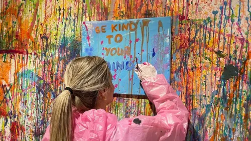 Person painting on canvas with colorful splatters.