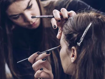 Make-up artist applies makeup to another person in a studio.