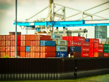 Containers are piled up under cranes in the harbor.