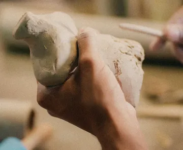 Hands holding and shaping clay object.