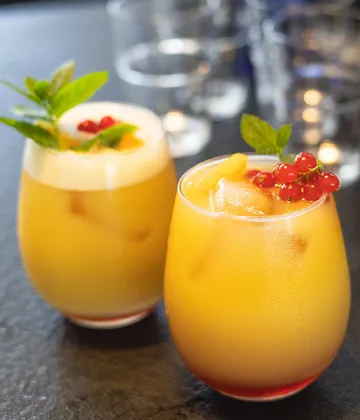 Two cocktails with fruit garnish on table.