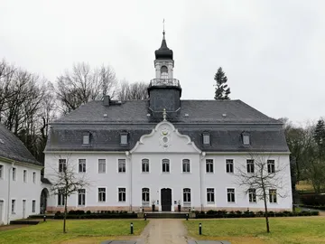 Historisches Gebäude mit Turm, umgeben von Bäumen.