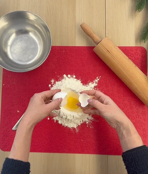Hands cracking egg into flour on table.