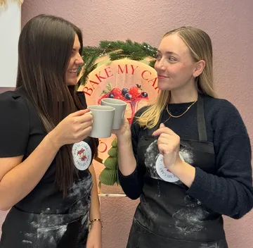 Zwei Frauen stoßen mit Tassen in Küche an.