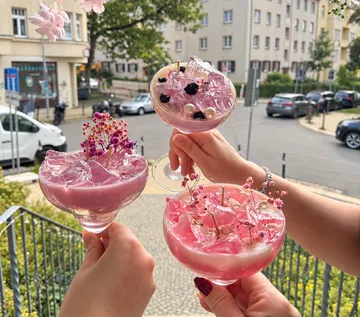 Drei Hände halten rosa Cocktails im Freien.