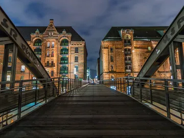 Wooden bridge connects historic brick buildings at night.