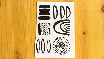 Paper with black abstract shapes on table.