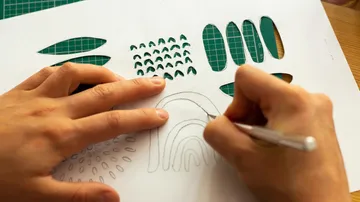 Hands cutting paper on green cutting mat.