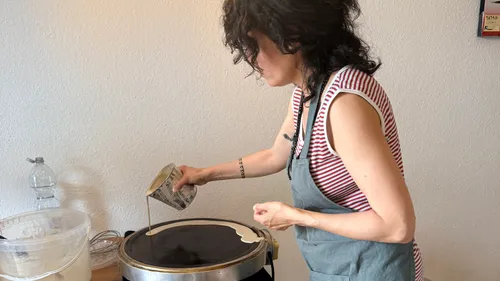 Person gießt Teig auf Crêpe-Pfanne drinnen.