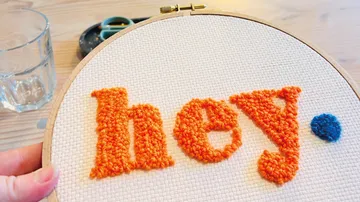 Stickrahmen mit orangefarbenem Text auf Tisch.