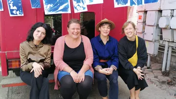 Four women sitting, smiling by red wall.