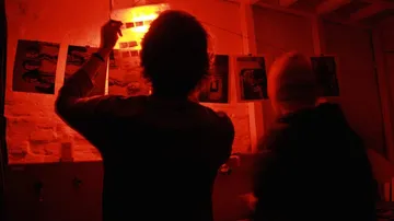 People developing photos in darkroom with red light.
