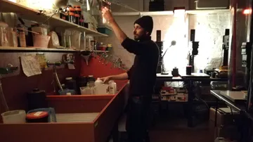 Person developing film in darkroom, shelves around.