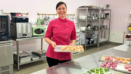 Chef holding tray of baked macarons in kitchen.