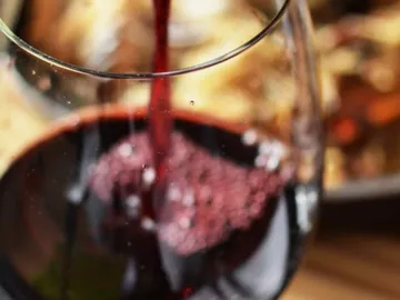 Red wine is poured into a glass surrounded by food.
